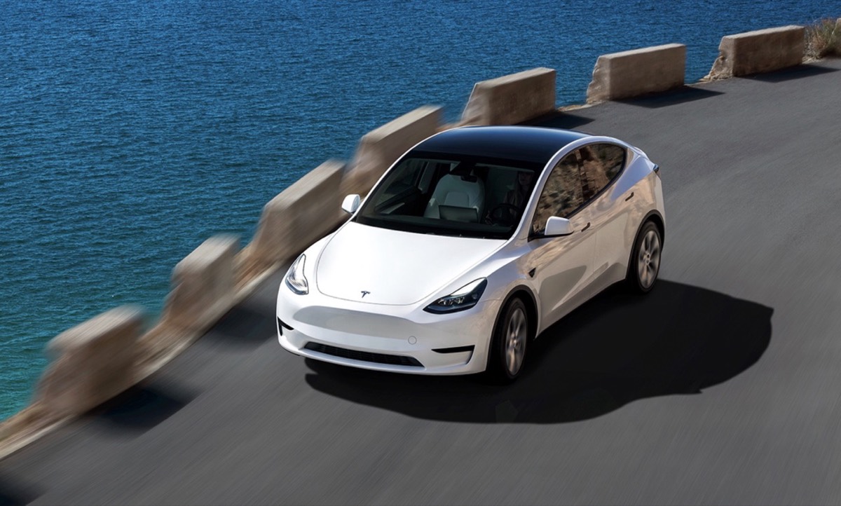 Bílá Tesla Model Y na pobřežní silnici